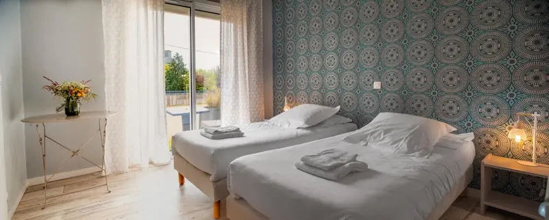 Chambre lumineuse avec deux lits simples et vue sur l'extérieur.
