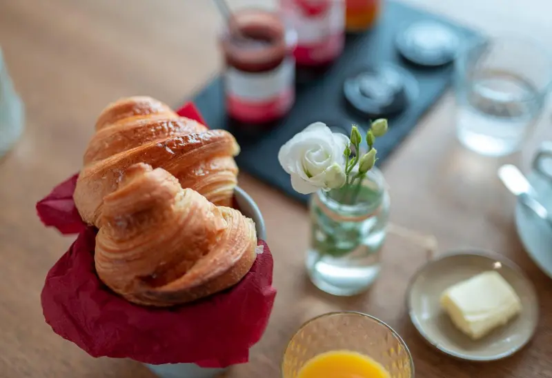 Une table présente des viennoiseries, des confitures et une fleur.
