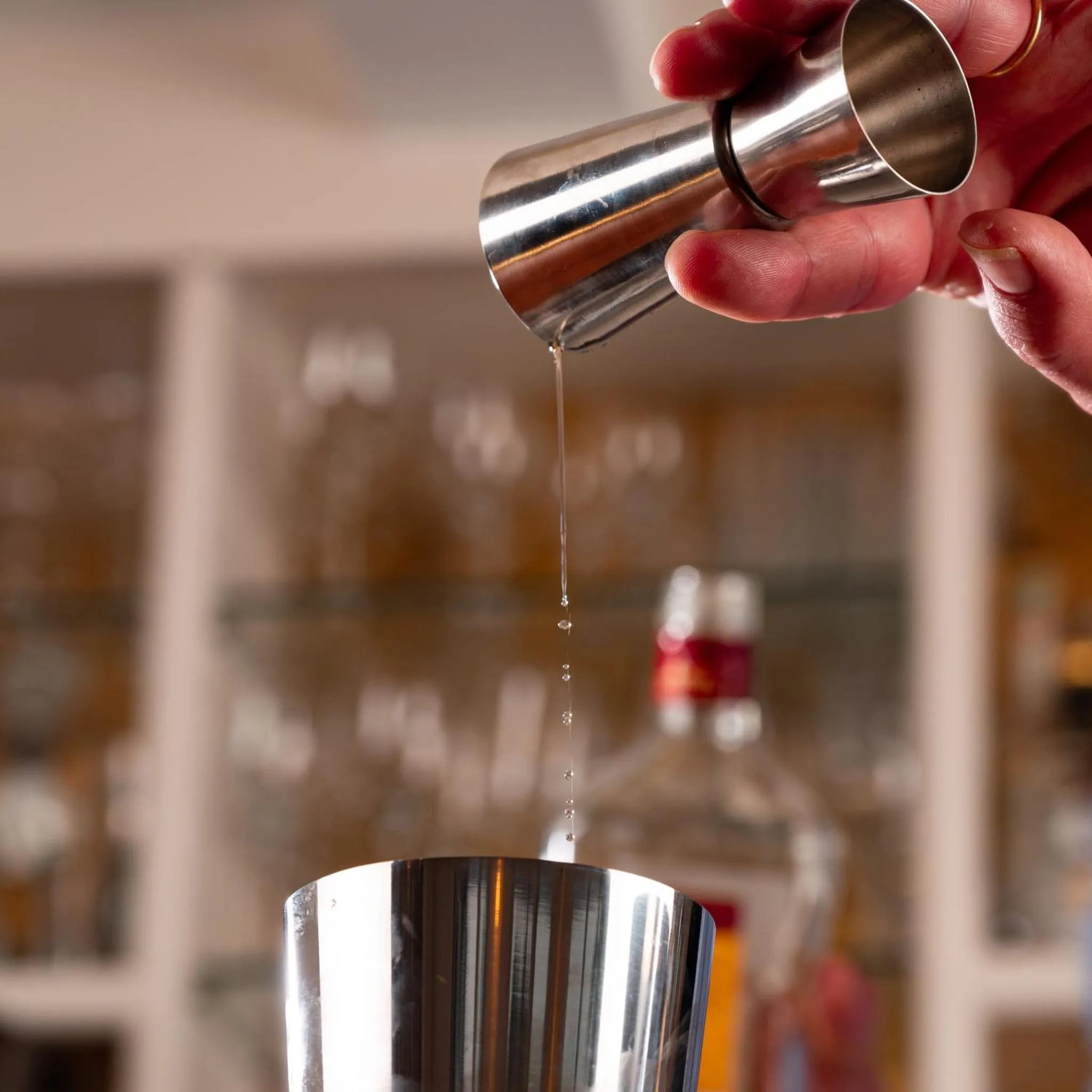 Un liquide transparent est versé d'un doseur en métal dans un verre.