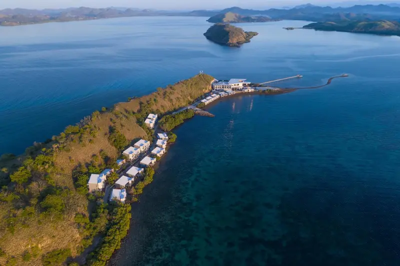 Vue aérienne d'un complexe hôtelier sur une presqu'île rocheuse bordée de mer turquoise.