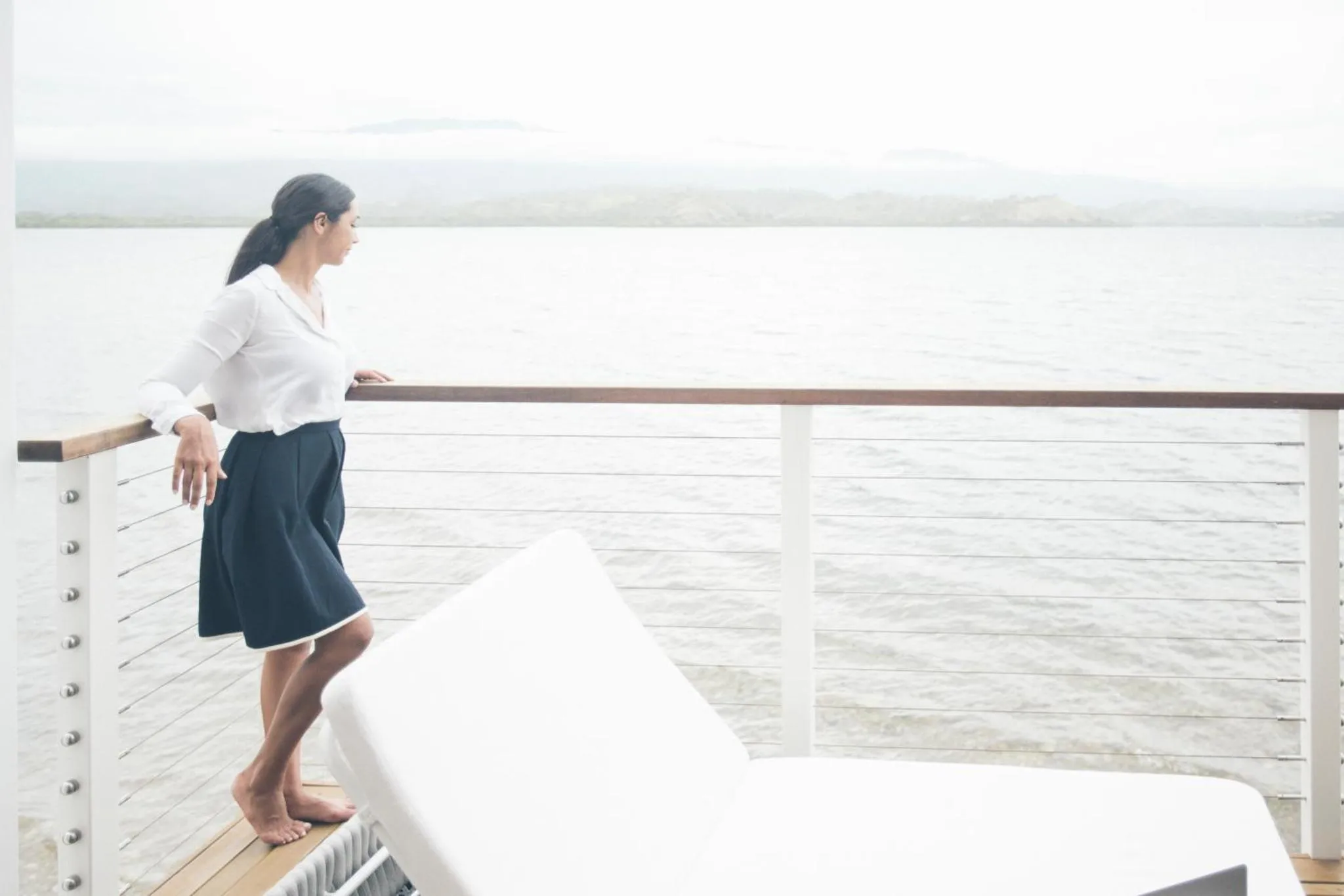 Une femme se tient debout sur une terrasse en bois face à la mer.