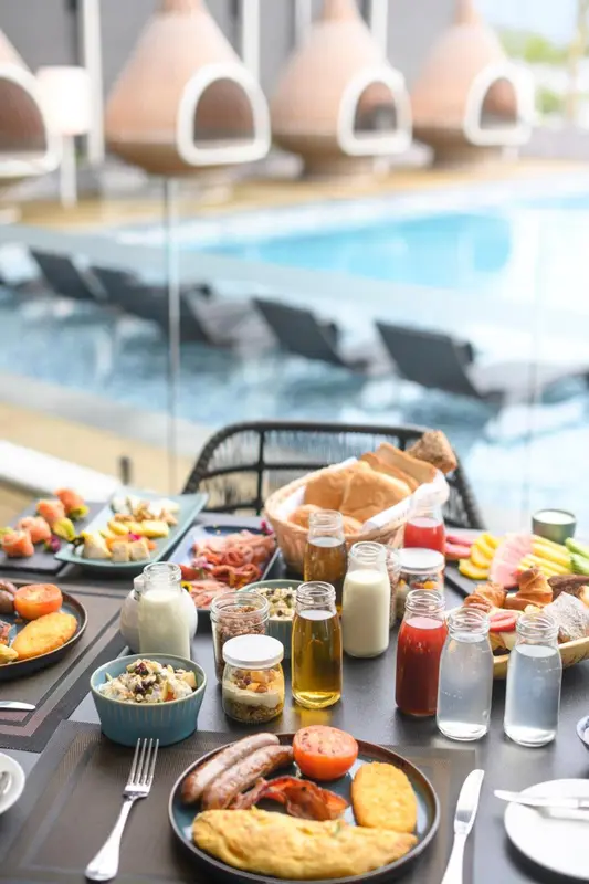 Une table est dressée avec un copieux petit-déjeuner face à une piscine.