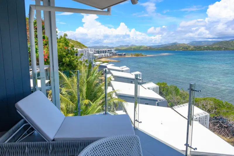 Deux transats blancs sur une terrasse avec vue sur la mer et les collines verdoyantes.