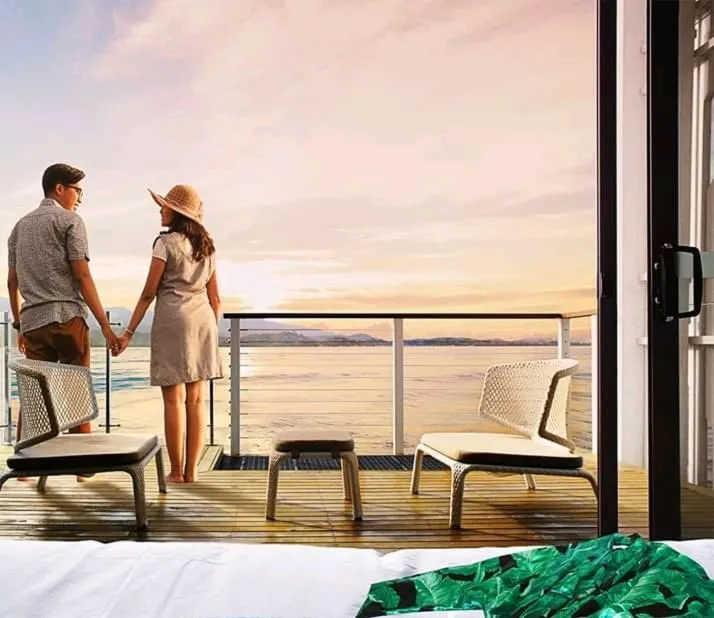 Un couple se tient la main sur une terrasse face à la mer au coucher du soleil.