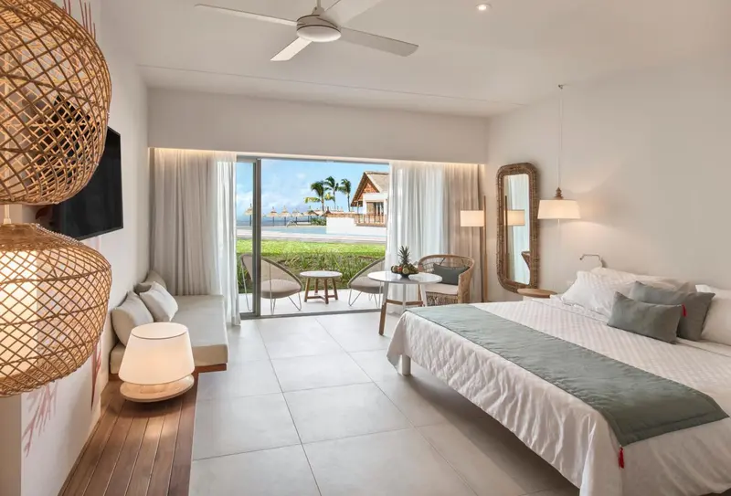 Une chambre lumineuse avec un lit fait et un coin salon donnant sur une vue sur la mer.