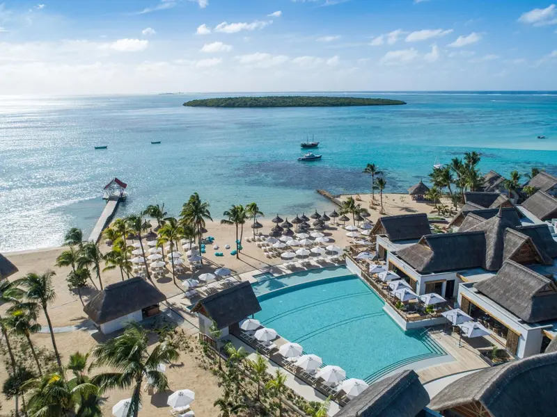 Vue aérienne d'une plage bordée de palmiers et d'une piscine turquoise.
