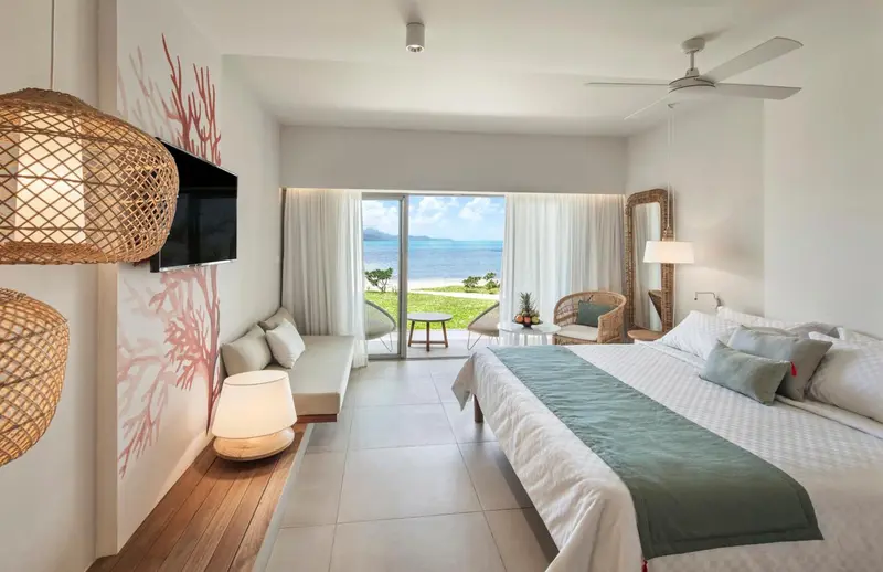 Une chambre lumineuse avec un grand lit et un canapé face à une baie vitrée donnant sur la mer.