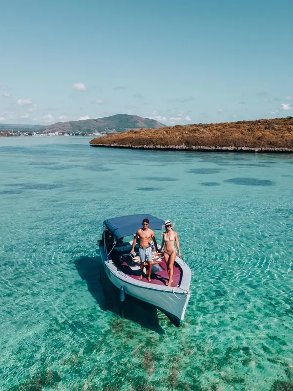 Un couple se tient sur la proue d'un bateau naviguant dans une eau turquoise claire.
