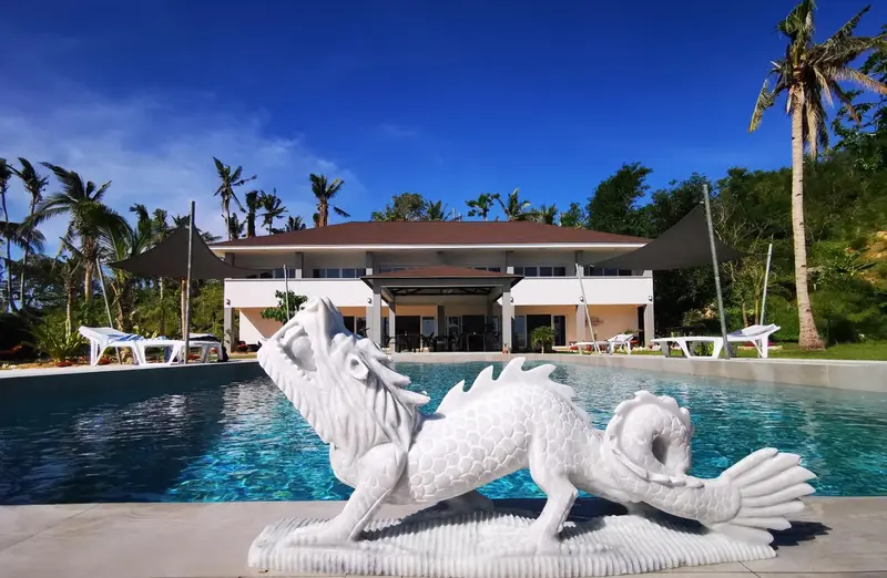 Une piscine avec une sculpture de dragon en son centre, devant un bâtiment blanc.