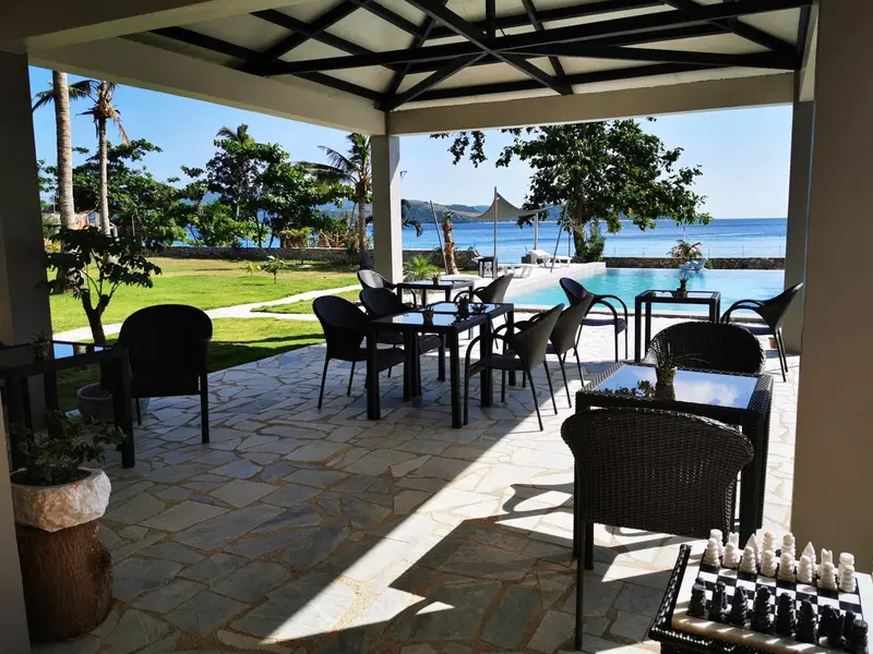 Terrasse ombragée avec tables et chaises donnant sur une piscine et la mer.