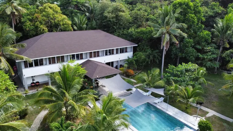 Bâtiment blanc avec toiture sombre surplombant une piscine et une végétation luxuriante.