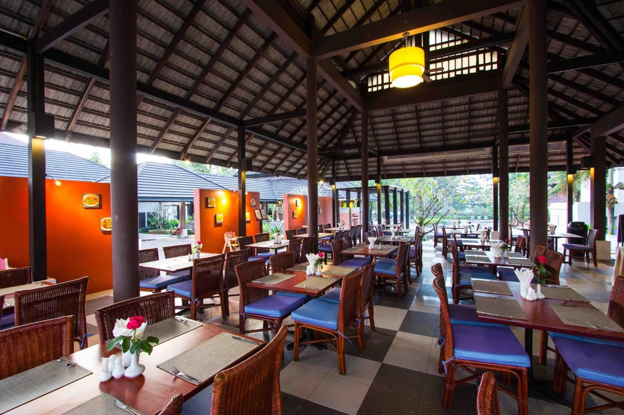 Une salle à manger extérieure avec des tables dressées et des chaises en osier.