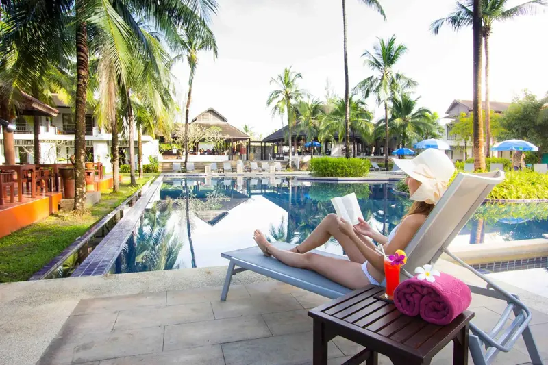 Une femme se relaxe au bord d'une piscine en lisant un livre.
