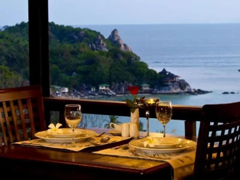 Table dressée avec des verres de vin et une vue sur la mer et les rochers.