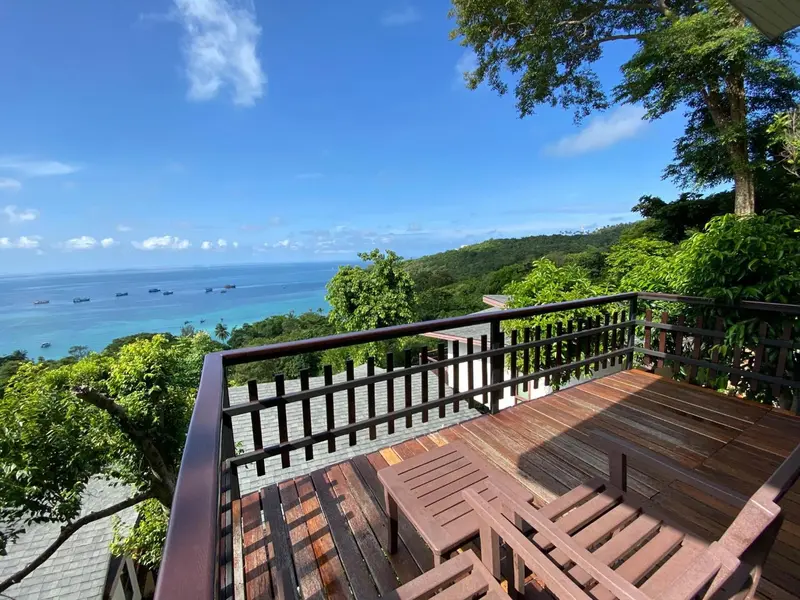 Terrasse en bois avec mobilier donnant sur une vue panoramique de la mer et de la végétation.