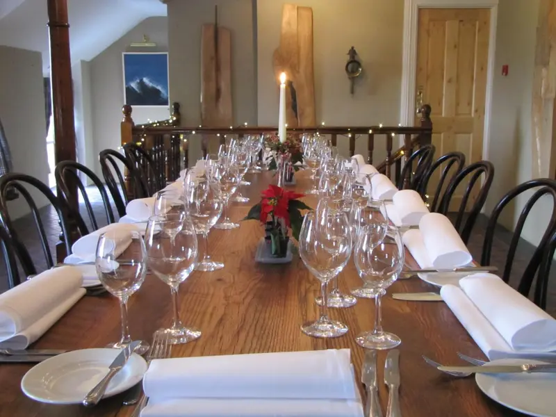 Une longue table en bois est dressée pour un repas avec des couverts et des verres.