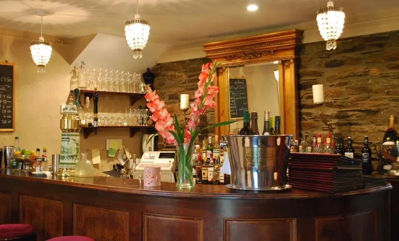 Un comptoir de bar en bois sombre est décoré de fleurs et de bouteilles.