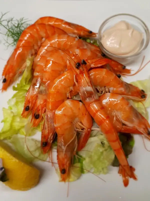 Assiette de crevettes roses servies avec une sauce et des légumes.