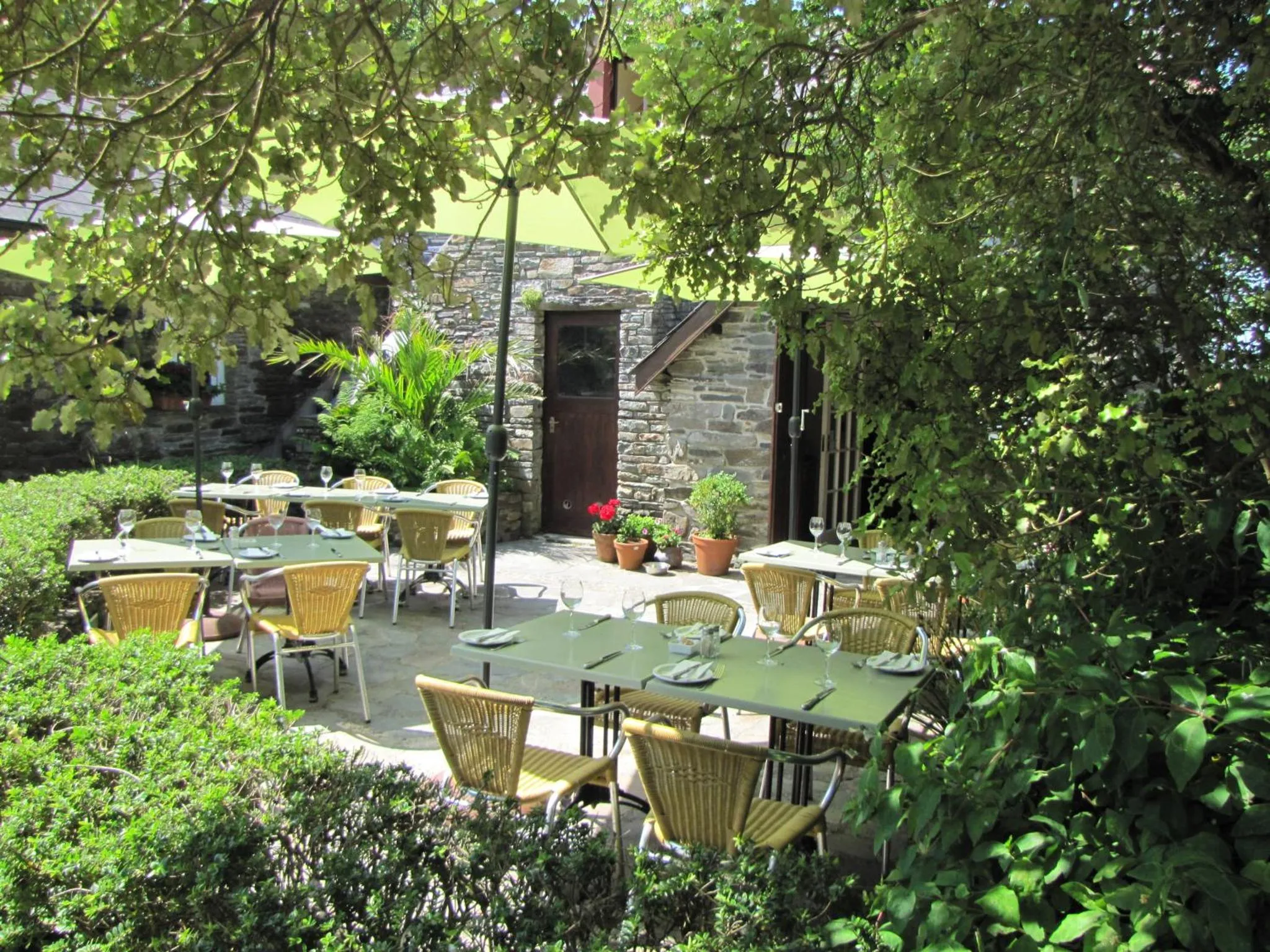 Terrasse ombragée avec tables et chaises en osier.