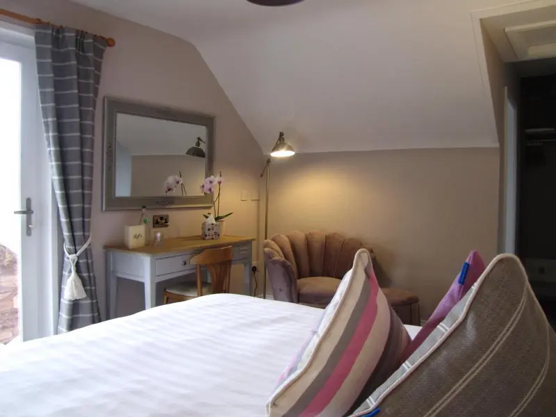 Une chambre lumineuse avec un lit, un bureau et un fauteuil.