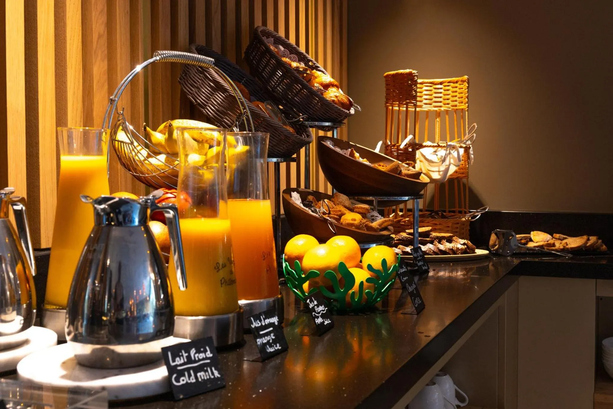 Un buffet propose des jus d'orange, des viennoiseries et des fruits frais.