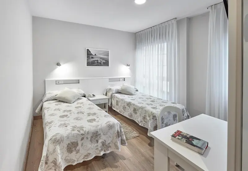 Chambre lumineuse avec deux lits simples et décoration sobre.