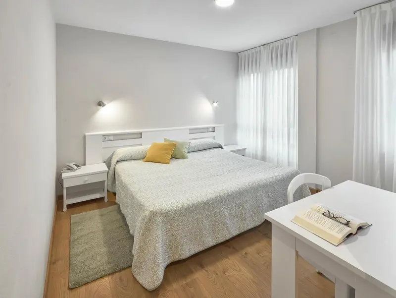 Une chambre lumineuse avec un grand lit recouvert d'une couverture et un bureau.