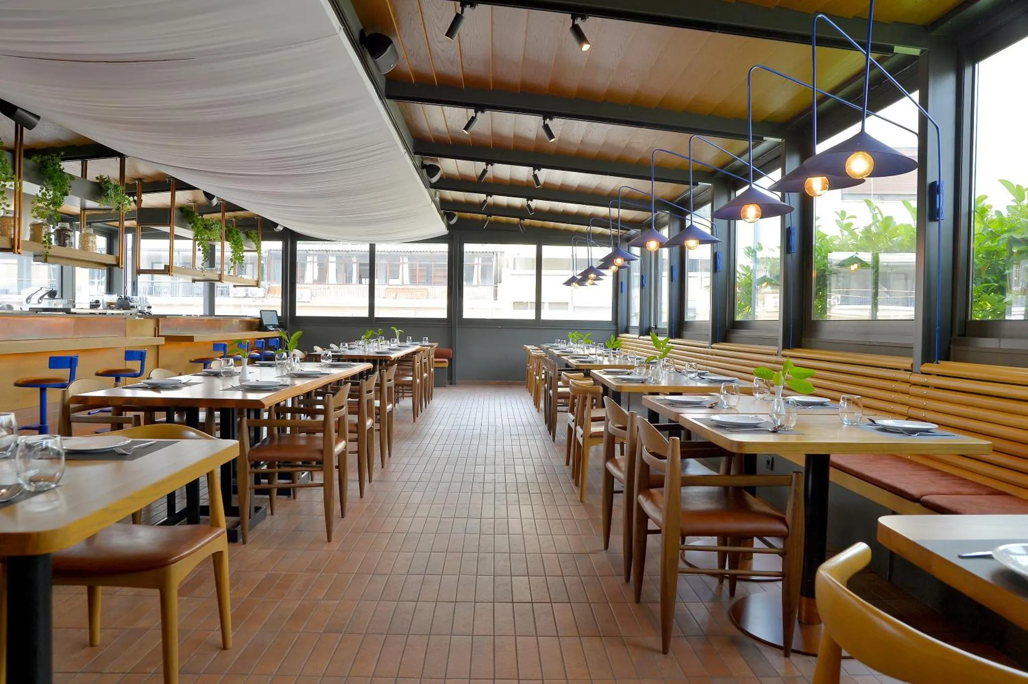 Une salle de restaurant lumineuse avec des tables dressées et des suspensions décoratives.