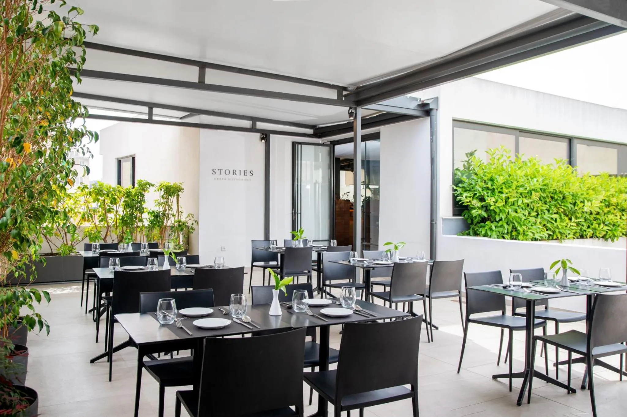 Terrasse ombragée avec tables et chaises noires prêtes pour le service.
