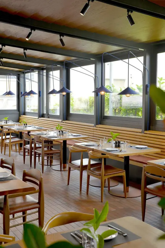 Une salle de restaurant lumineuse avec des tables dressées et des suspensions.