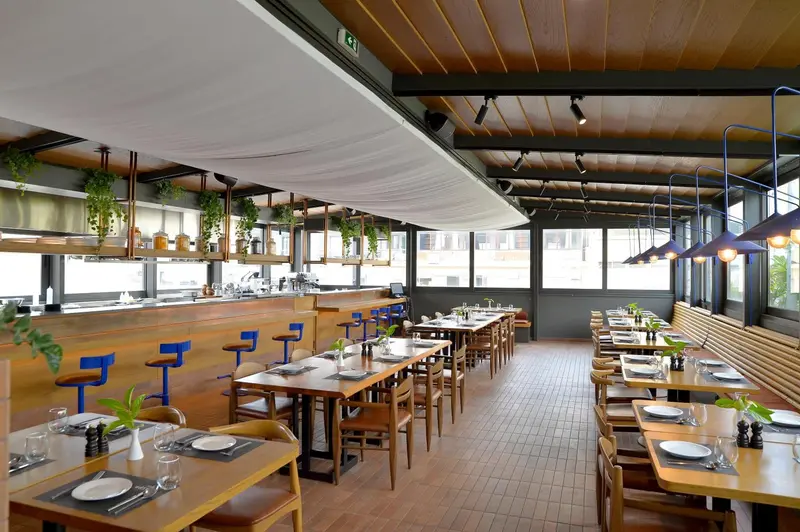 Une salle de restaurant lumineuse avec des tables dressées et un comptoir de bar.