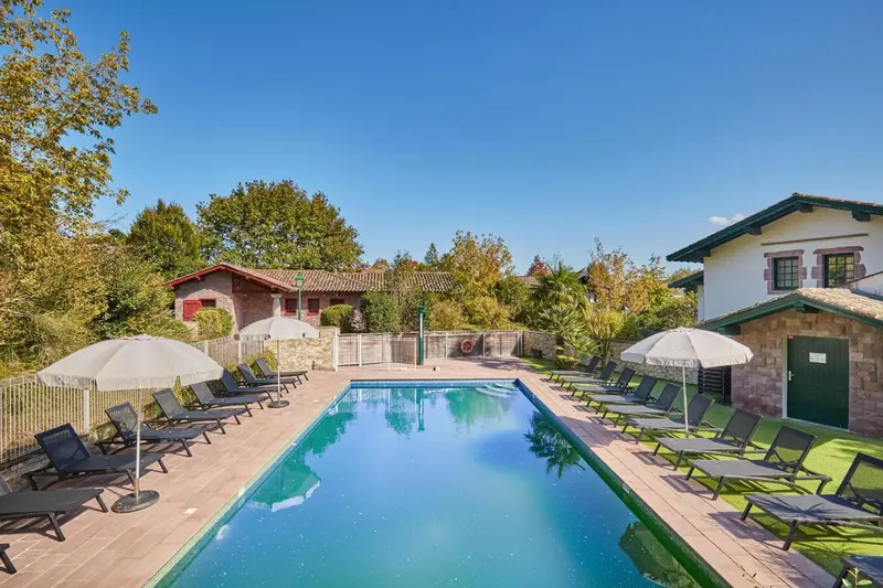 Une piscine rectangulaire bordée de transats sous des parasols blancs.