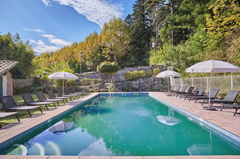 Une piscine rectangulaire bordée de transats sous des parasols blancs.