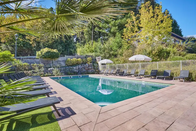 Une piscine rectangulaire entourée de chaises longues et de végétation luxuriante.