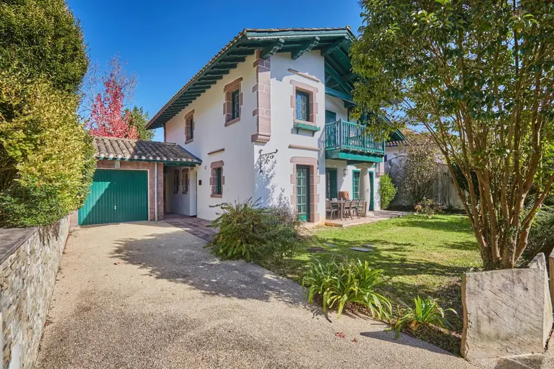 Maison blanche avec des volets verts et un jardin soigné.