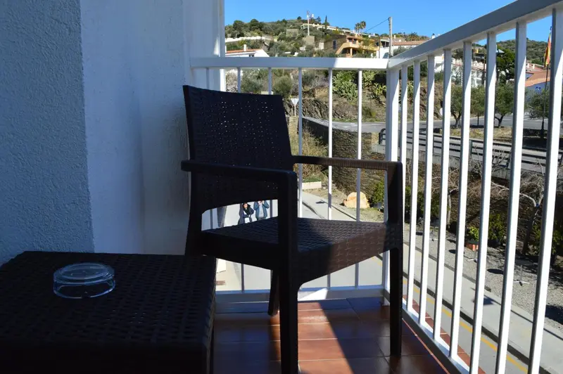 Une terrasse avec une chaise et une petite table offre une vue sur la végétation et les bâtiments environnants.