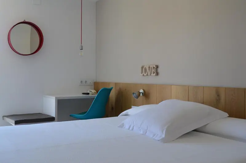 Une chambre lumineuse avec un lit blanc et un bureau bleu turquoise.
