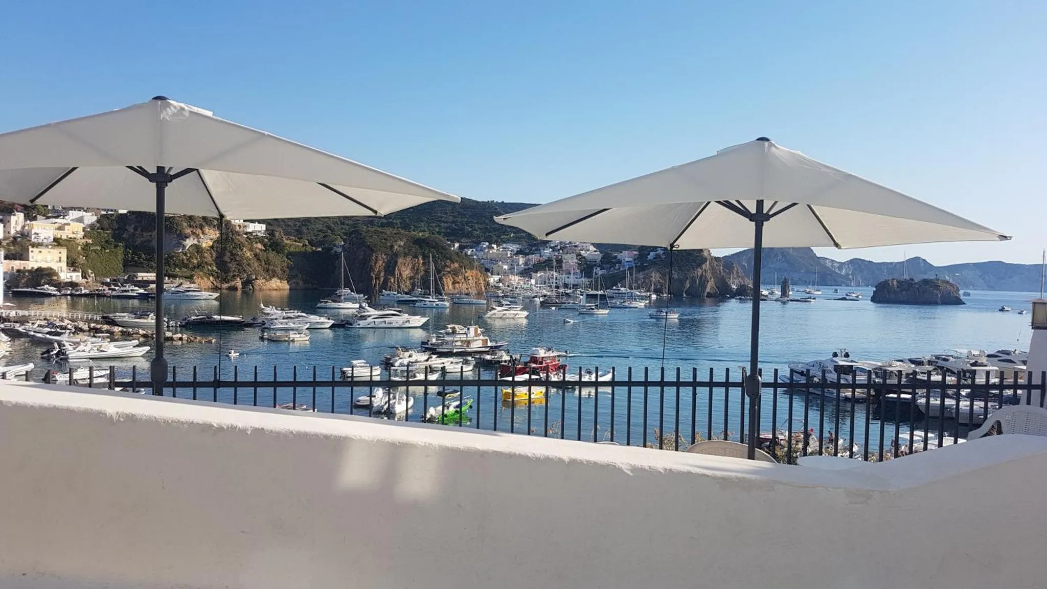 Terrasse ombragée donnant sur un port de plaisance ensoleillé.