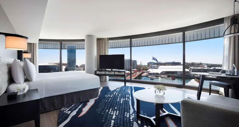 Chambre lumineuse avec un grand lit et une vue sur la ville.