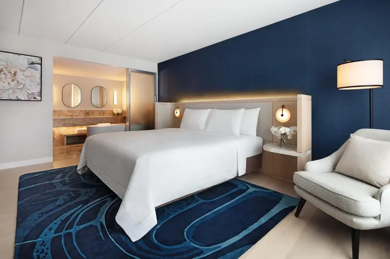 Chambre lumineuse avec un grand lit et un fauteuil.
