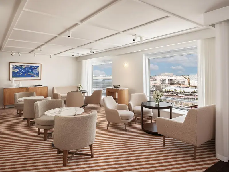 Espace de détente lumineux avec des fauteuils et tables basses, donnant sur une vue urbaine.