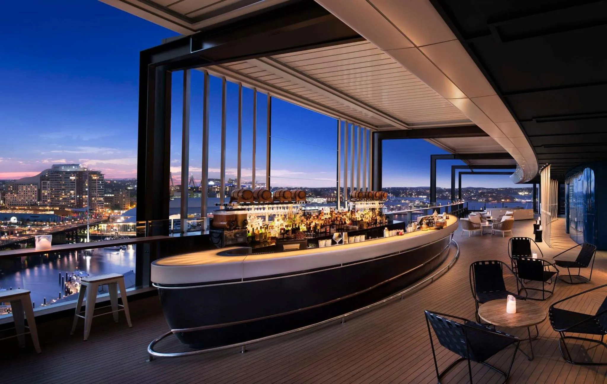 Un bar en terrasse offre une vue panoramique sur une ville illuminée au crépuscule.