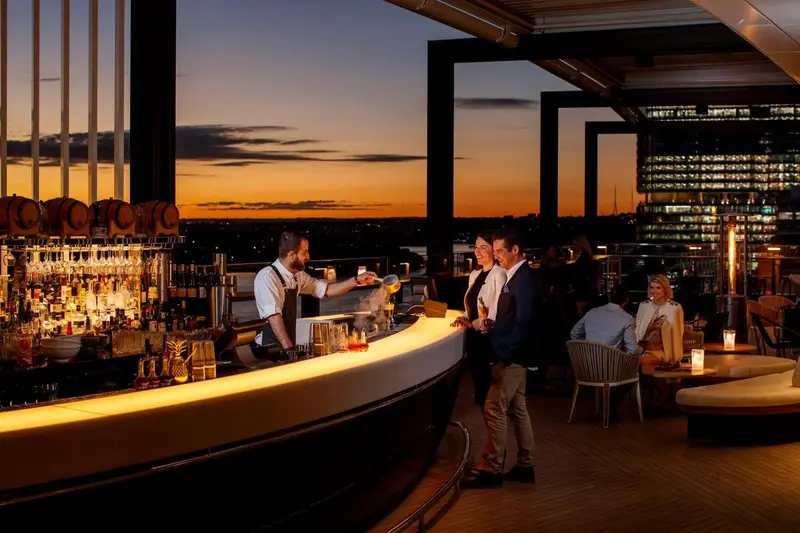Un bar en terrasse offre une vue sur la ville illuminée au coucher du soleil.