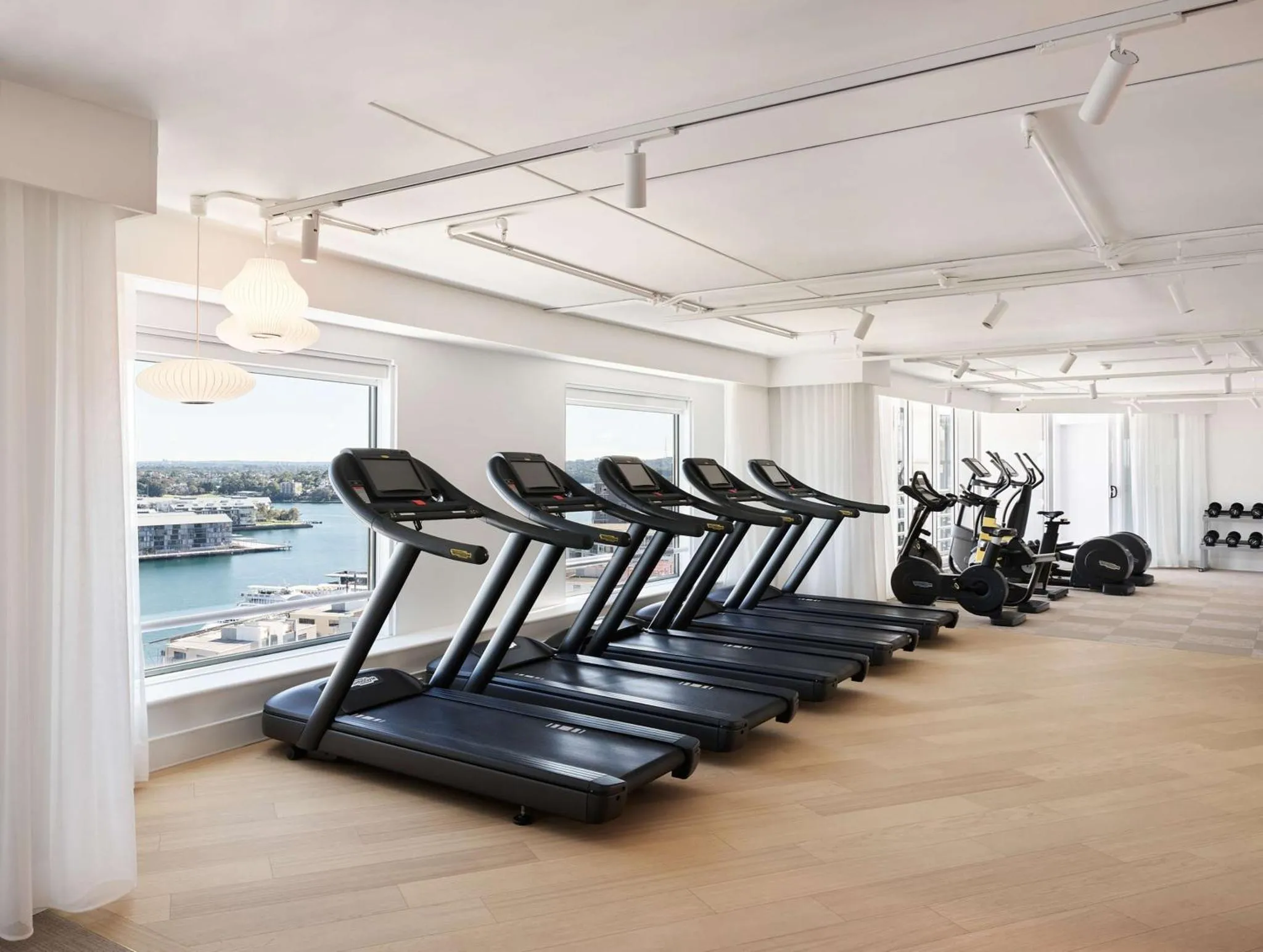 Une salle de sport lumineuse avec des tapis de course face à une vue sur la mer.