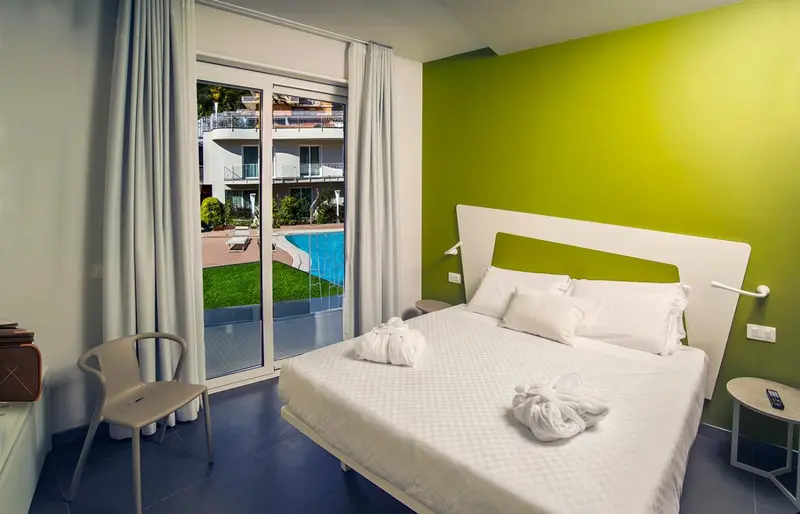 Chambre lumineuse avec un lit blanc et une vue sur une piscine.