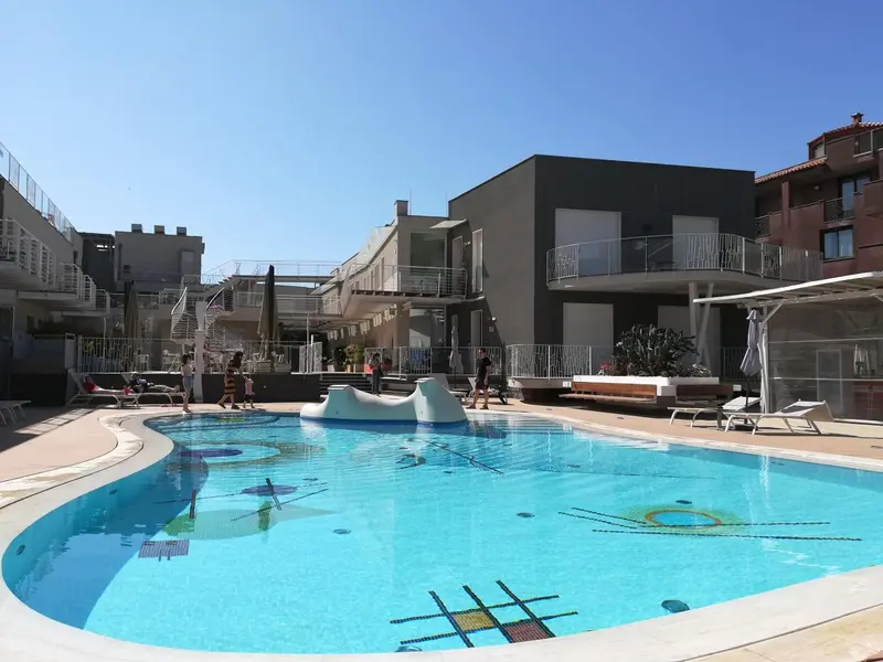 Piscine rectangulaire avec fontaine centrale et transats disposés autour.