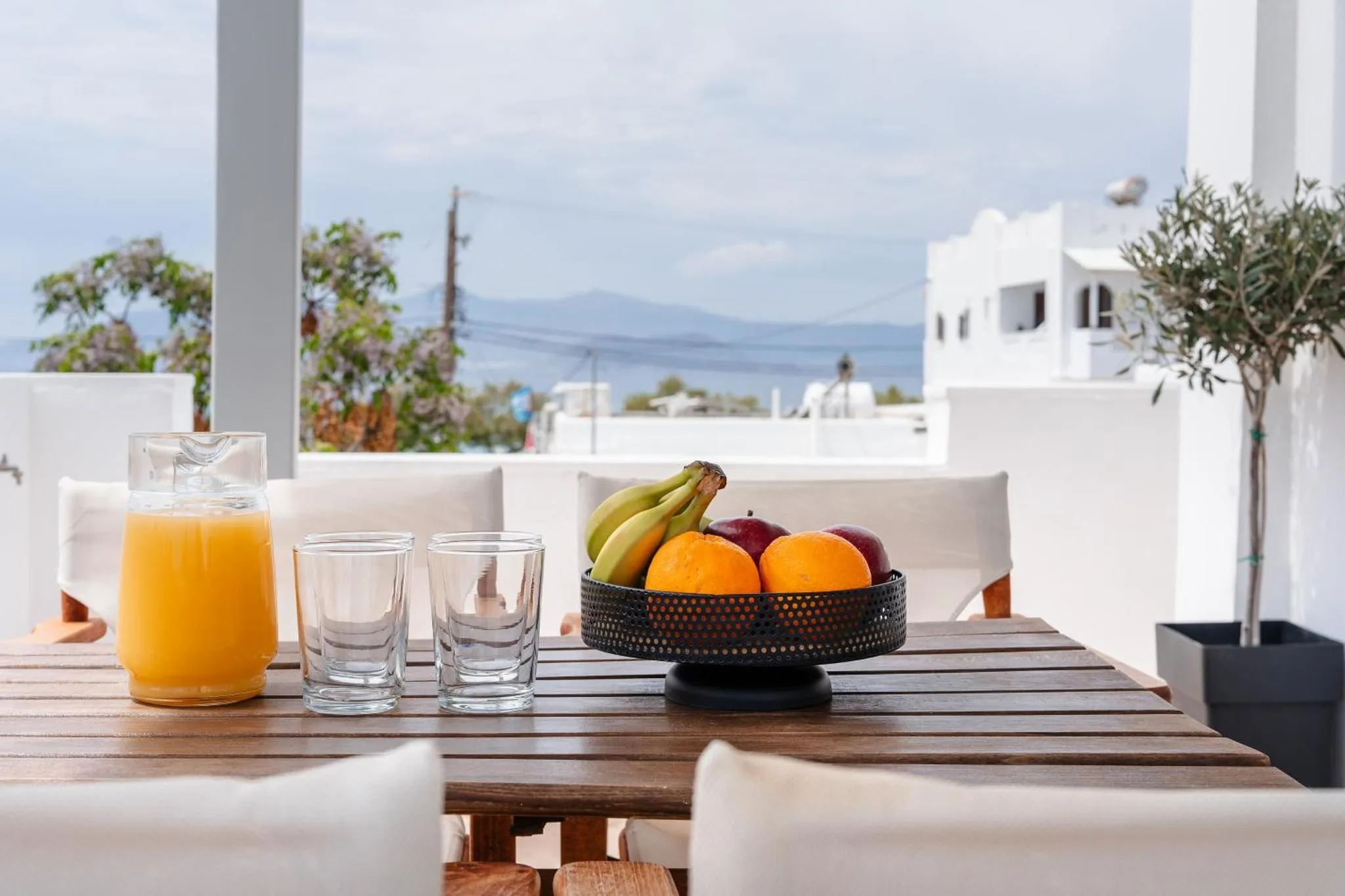 Une table en bois avec des fruits frais et des boissons sur une terrasse lumineuse.