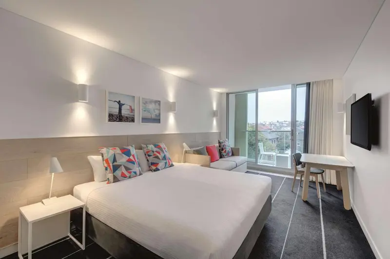 Chambre moderne avec un grand lit et un canapé près d'une fenêtre.