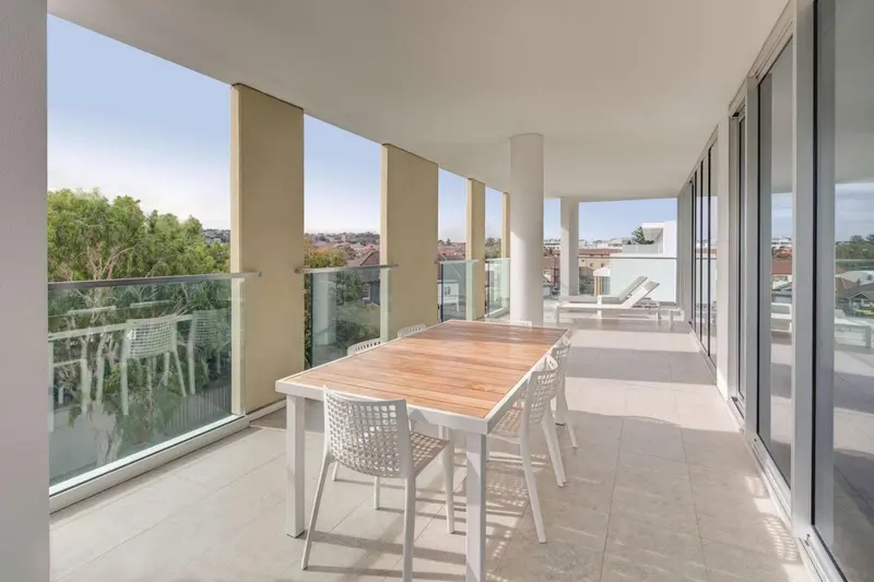 Une table et des chaises blanches sont disposées sur une terrasse carrelée.