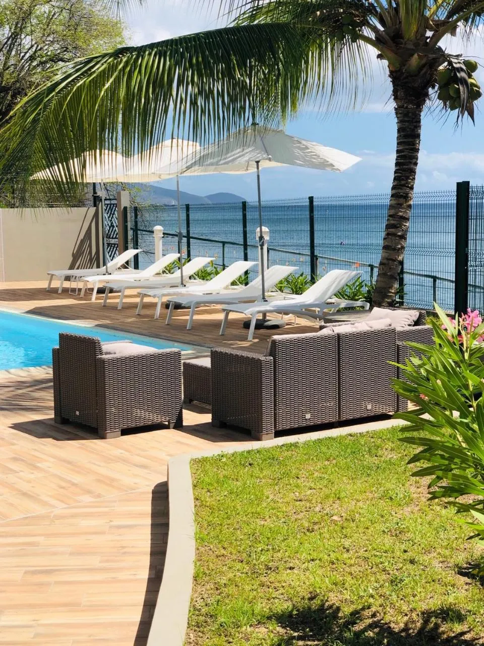 Transats blancs et mobilier de jardin près d'une piscine en bord de mer.